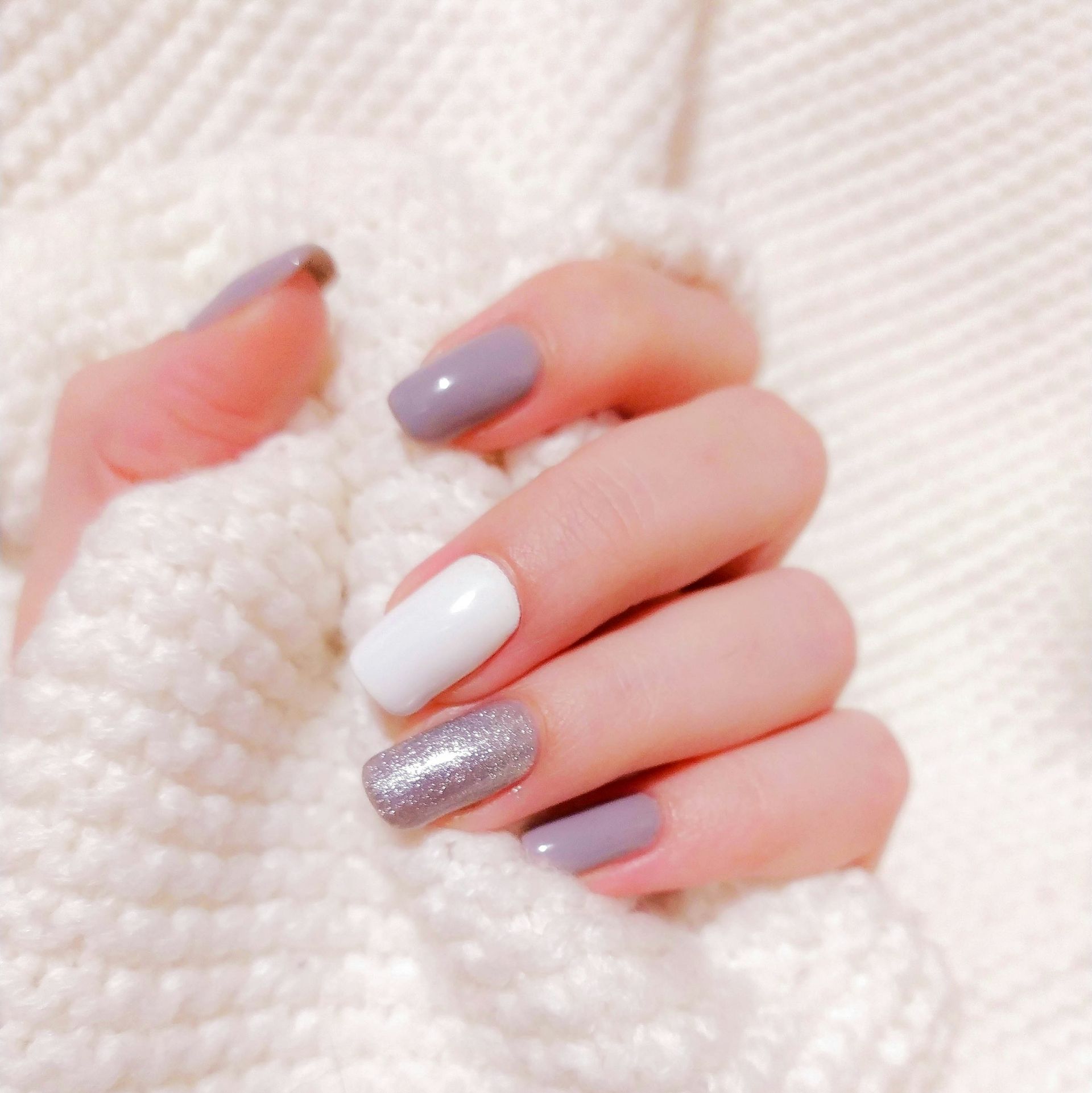 A hand with mauve, white, and silver glitter nails holding a white knit sweater